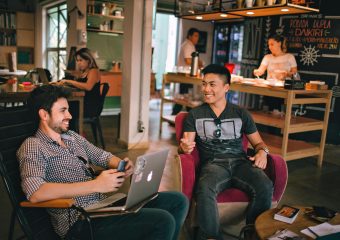 Two men enjoying a relaxed conversation with laptops in a cozy Brazilian café.