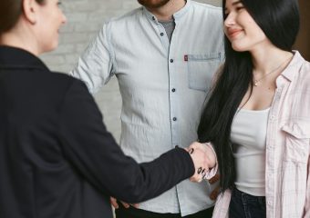 Three adults shaking hands in a professional meeting setting, showing agreement and positive interaction.