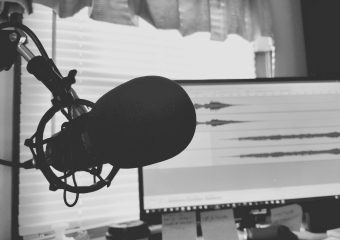 Black and white image of a podcast setup with microphone and waveform screen.